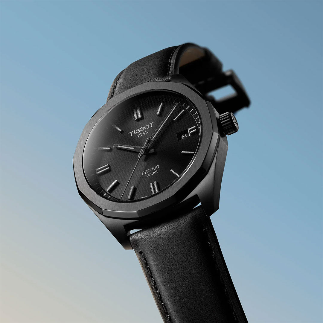 A sleek Tissot PRC 100 Solar Quartz 39mm watch is showcased on a gradient blue background, highlighting its modern black design and minimalist style—ideal for fans of the Tissot PRC 100 collection.