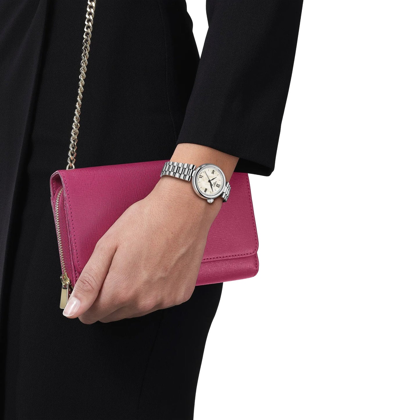 Dressed in black, a person holds a pink clutch with a gold chain strap and wears the Tissot Desir Quartz 28mm Watch, featuring a silver finish, domed case, and quartz movement.