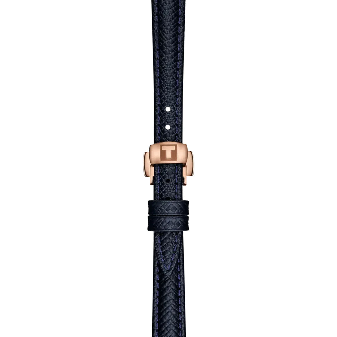 A close-up of the Tissot Desir Automatic 28mm Watch shows its dark textured leather strap with a rose gold T-engraved clasp, two loops, fine stitches, and an elegant blue mother-of-pearl dial.