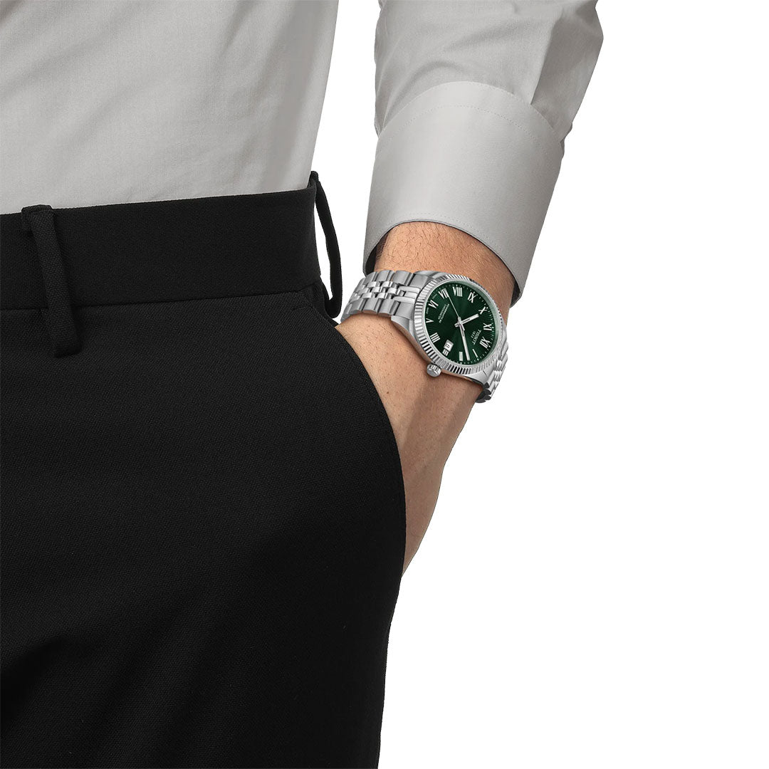 A person in black pants and a white dress shirt has their hand in their pocket, showcasing a Tissot Ballade Powermatic 80 Automatic 39mm watch with a green face on their left wrist.