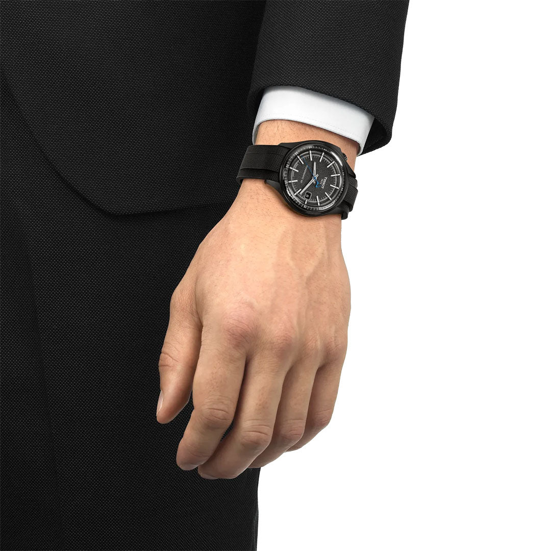A person in a black suit and white shirt is shown from the waist up, highlighting their left wrist with a Tissot Pinarello Mechanical Automatic COSC 43mm Watch, showcasing Swiss craftsmanship.