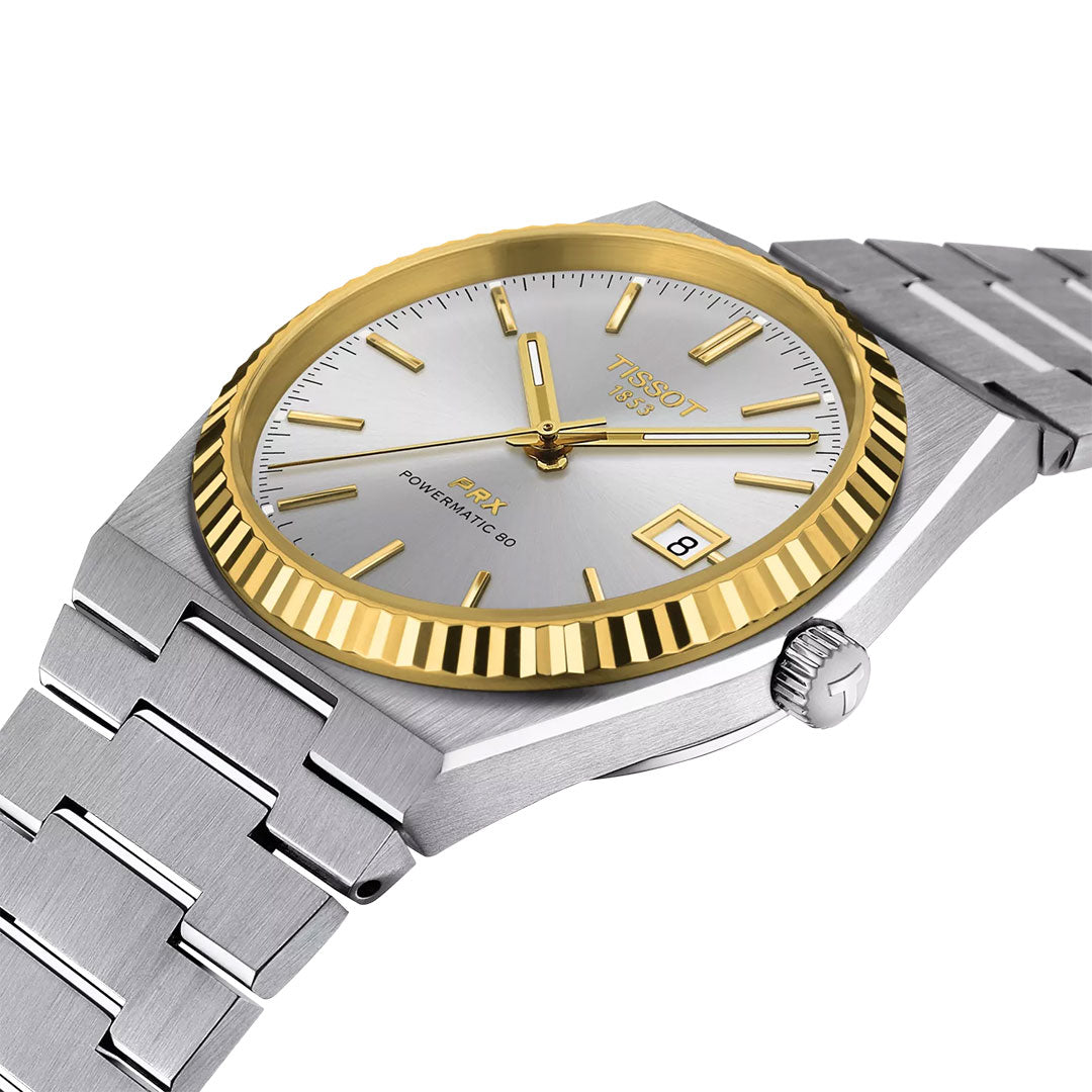 The Tissot PRX 18K Gold Powermatic 80 Automatic 40mm Watch features a silver dial, gold hour markers and hands, gold fluted bezel, date window at 3 o’clock, sapphire crystal, and a stainless steel bracelet.