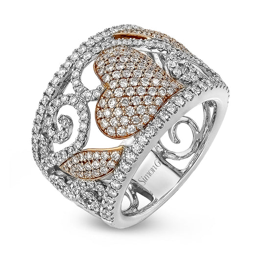 The Simon G. 18K White and Yellow Gold Diamond Fashion Ring is a sophisticated piece featuring an intricate filigree design with a central heart shape adorned with small sparkling diamonds and gold accents. The wide band, crafted in 18-karat gold, boasts detailed patterns that add an elegant touch to the design.