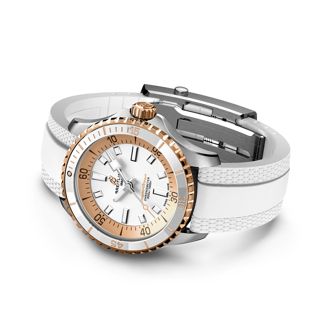 The BREITLING Superocean Automatic 36 by Breitling features a white face, gold accents, and rotating bezel. Its textured white strap is shown angled to display the face and clasp.