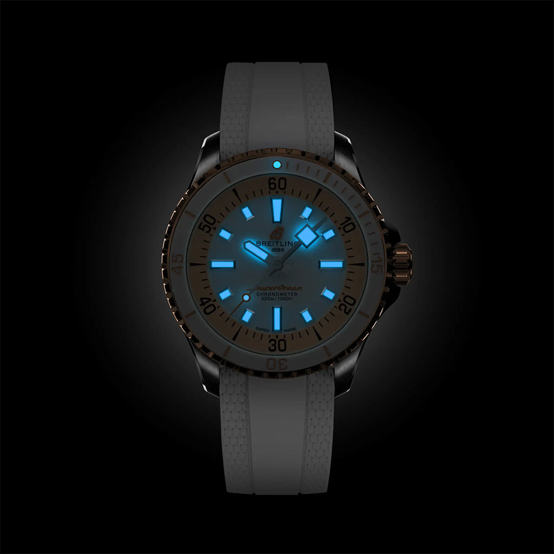 The BREITLING Superocean Automatic 36 by Breitling features a dark case with a light strap and glows blue in the dark, illuminating its hour markers, hands, and indices over a black background.