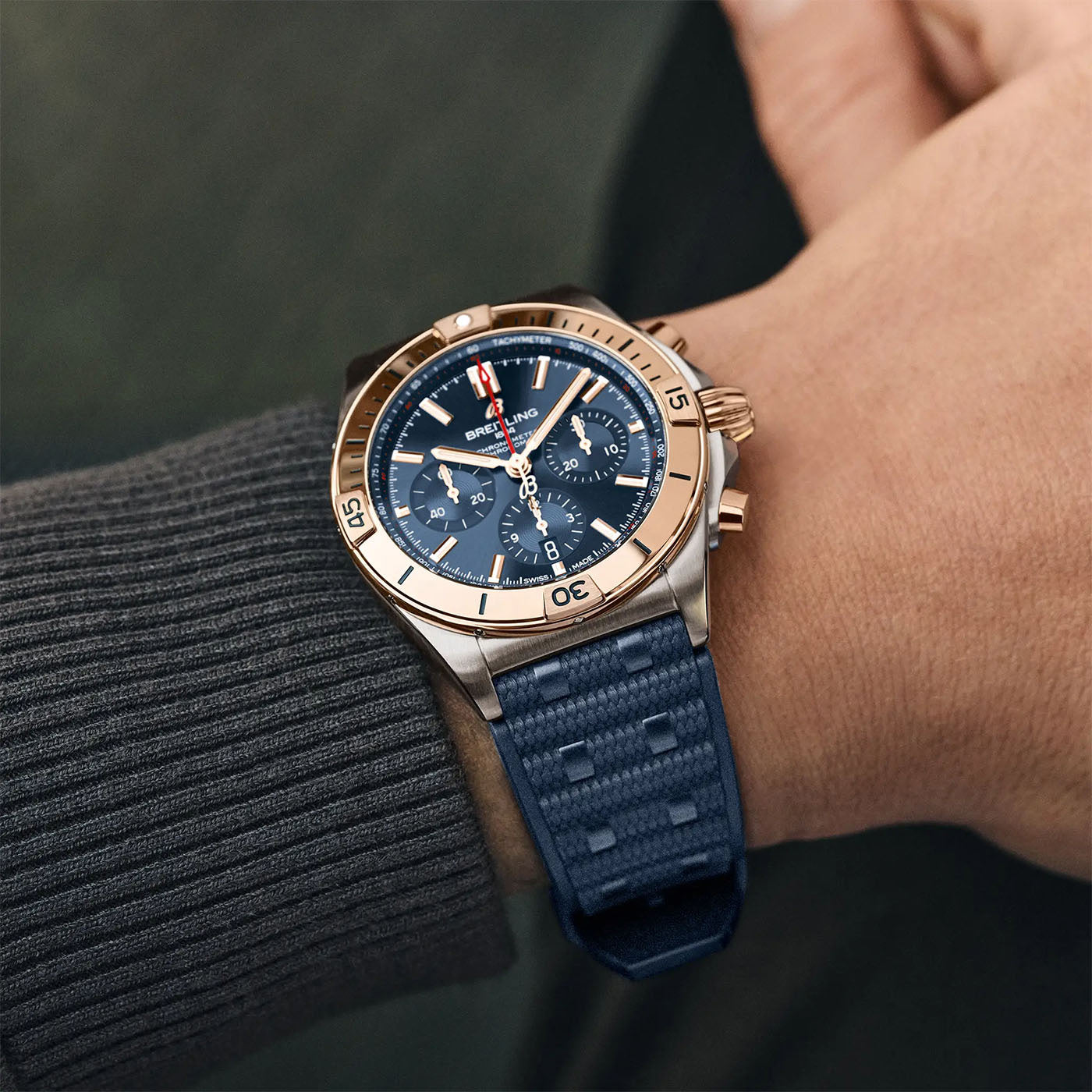 A person wearing the BREITLING Chronomat B01 42 by Breitling, showcasing a sophisticated wristwatch with a gold and silver bezel, blue dial featuring three subdials, and an aviation-inspired design. The watch embodies luxury and elegance with its classic look and blue textured strap.