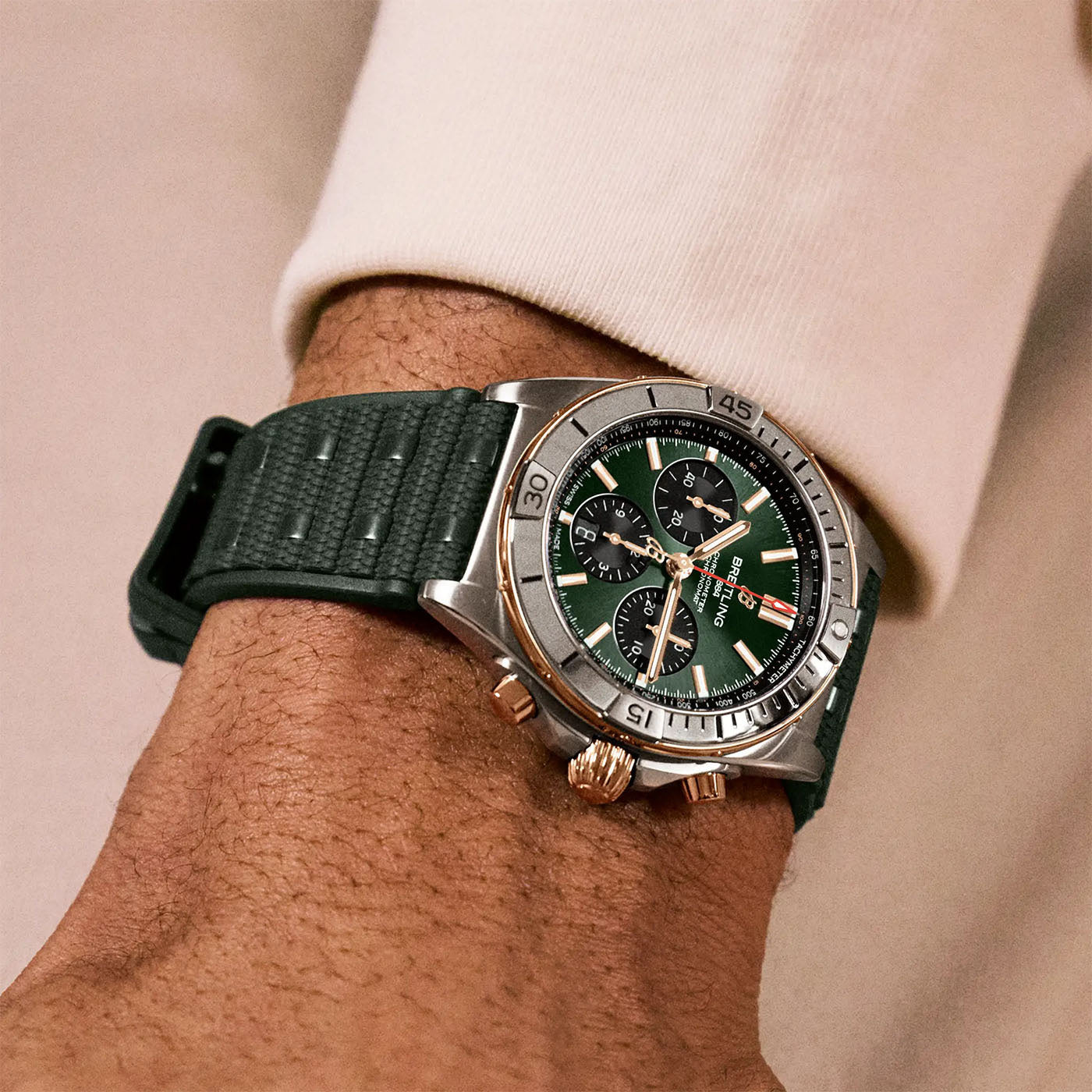 A person wearing the BREITLING Chronomat B01 42 on their wrist. This Breitling chronograph showcases a green face with multiple dials and is paired with a textured green strap, accentuated by the person's off-white long-sleeve sweater.