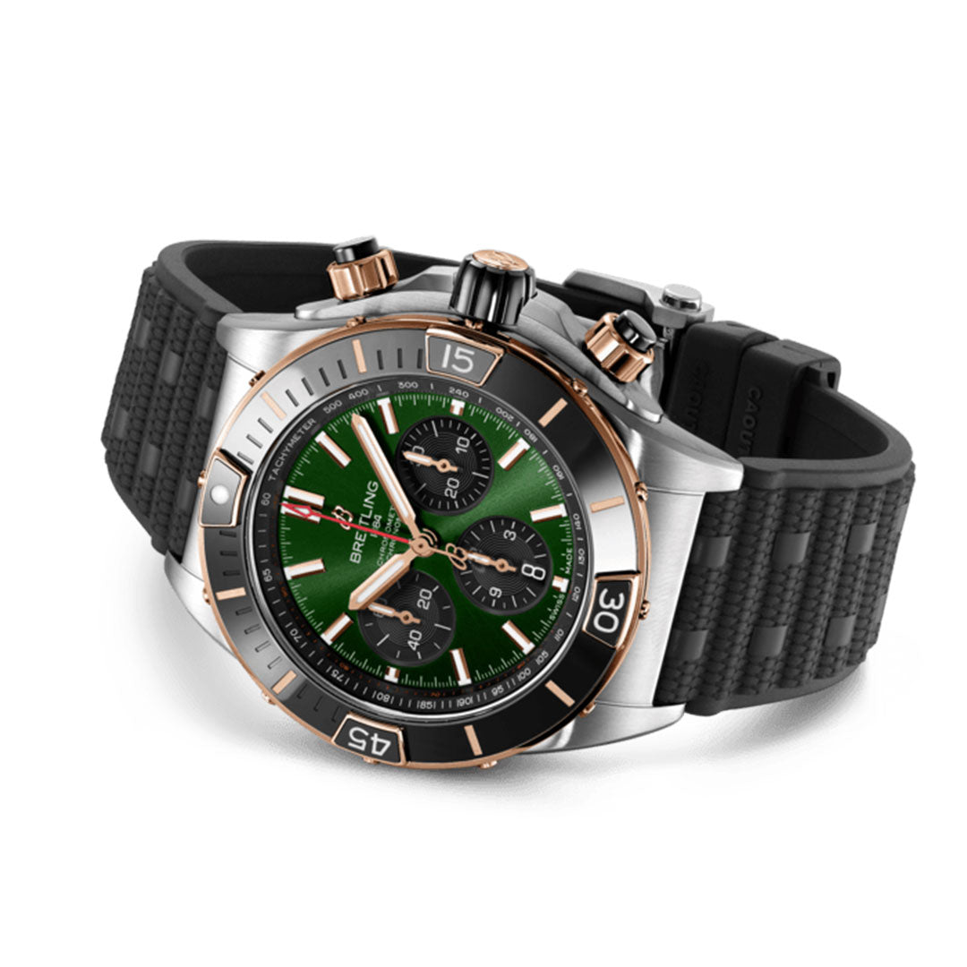 The BREITLING Chronomat B01 44 luxury wristwatch from Breitling showcases a green dial, three black subdials, and a black and gold rotating bezel. Complemented by its textured black rubber strap, this timepiece captures the essence of a Super Chronomat sports watch.