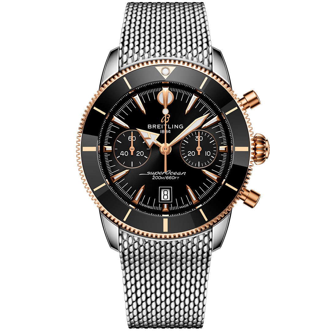 The BREITLING Superocean Heritage B01 Chronograph 42 features a black dial with gold accents, three subdials, date window, silver mesh strap, and gold crown/pushers. Powered by the Breitling Manufacture Caliber 01 dive chronograph movement.