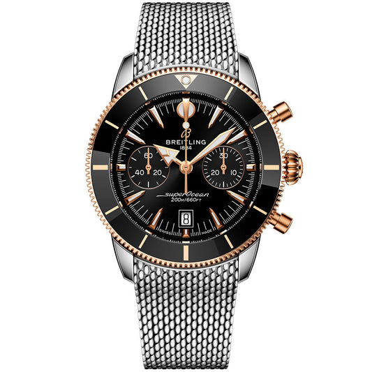 The BREITLING Superocean Heritage B01 Chronograph 42 features a black dial with gold accents, three subdials, date window, silver mesh strap, and gold crown/pushers. Powered by the Breitling Manufacture Caliber 01 dive chronograph movement.