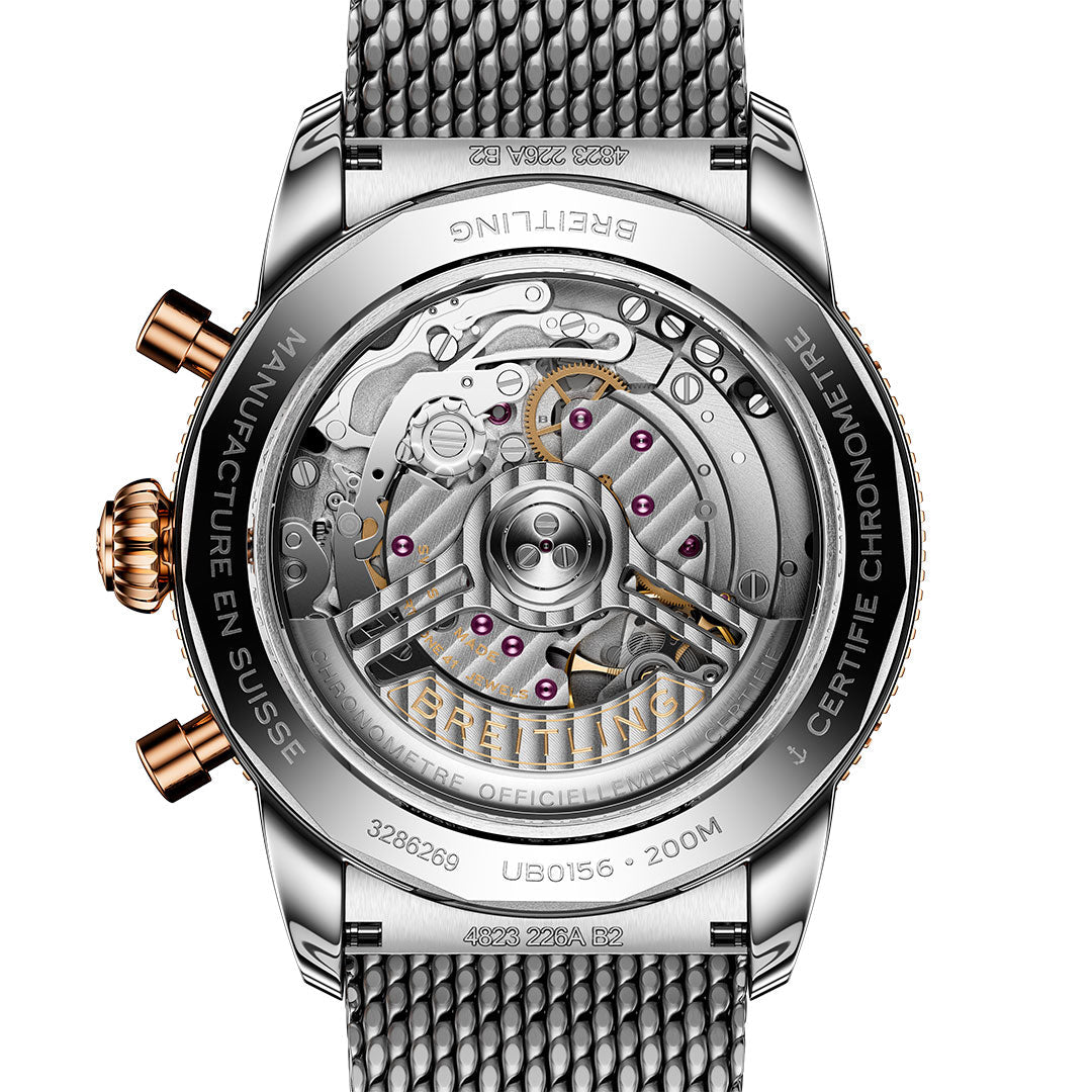 Close-up of the BREITLING Superocean Heritage B01 Chronograph 42 showcasing the Breitling Manufacture Caliber 01 through a transparent caseback, with inscribed details and a metal mesh bracelet.