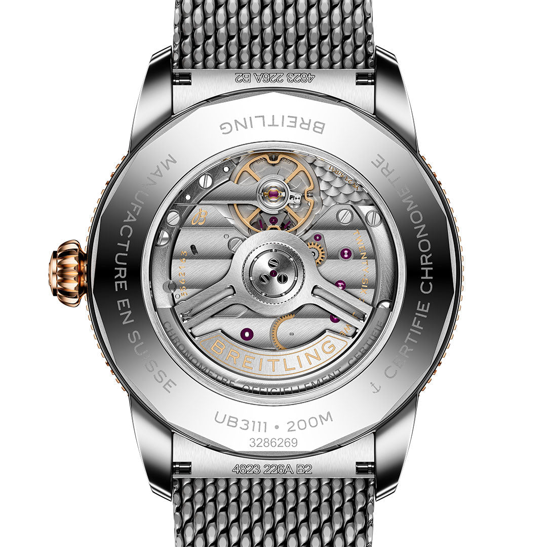 Close-up of the back of the BREITLING Superocean Heritage B31 Automatic 42, highlighting its exposed automatic movement, detailed gears, silver case with engraved branding, and mesh metal strap by Breitling.