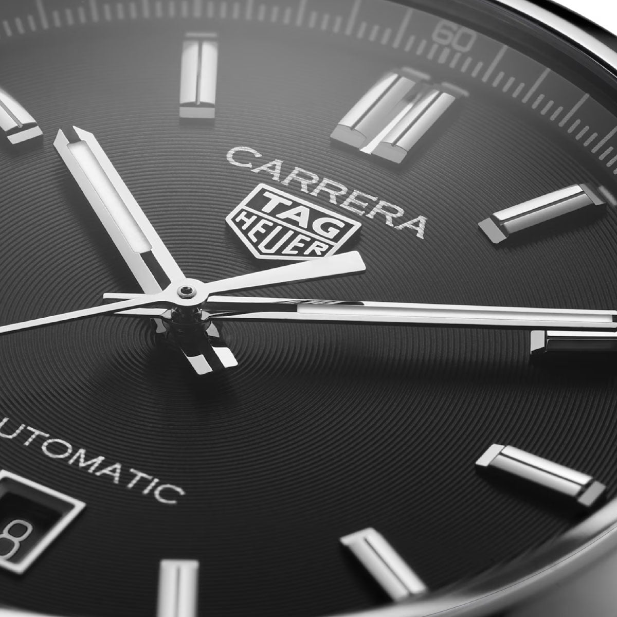 Close-up of the TAG Heuer Carrera Date Automatic 39mm watch face in black, featuring silver hour markers, hands, and the TAG Heuer logo. The word “AUTOMATIC” and a partial date window appear at the bottom left, showcasing the precision of its Calibre 5 Automatic movement in this elegant timepiece.