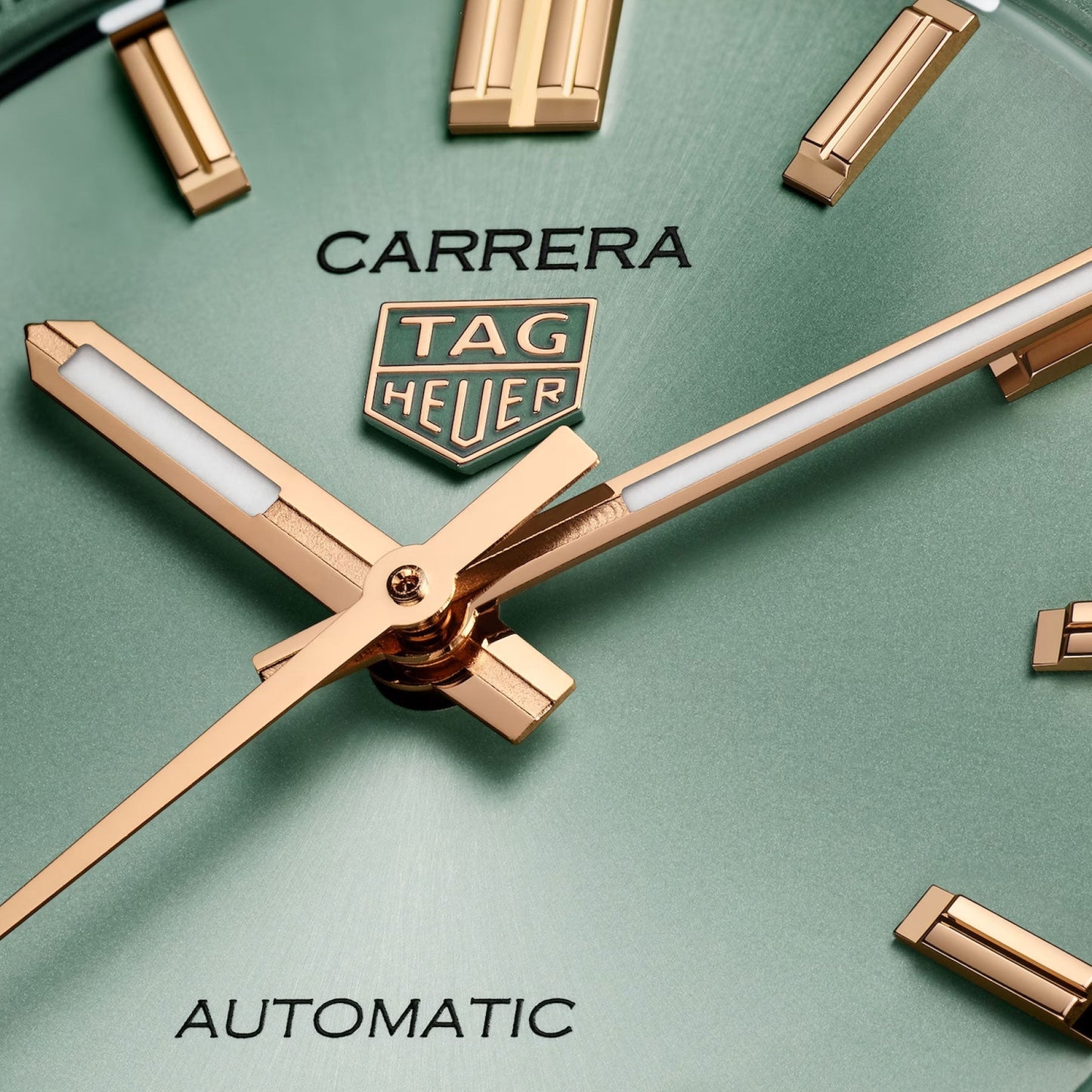 Close-up of the TAG Heuer Carrera Date Automatic 36mm watch face with a green background, gold hands, and gold hour markers, featuring the words “CARRERA,” “TAG HEUER,” and “AUTOMATIC” on the dial. This refined timepiece highlights the elegance of TAG Heuer’s craftsmanship, seamlessly complemented by a sleek steel bracelet.