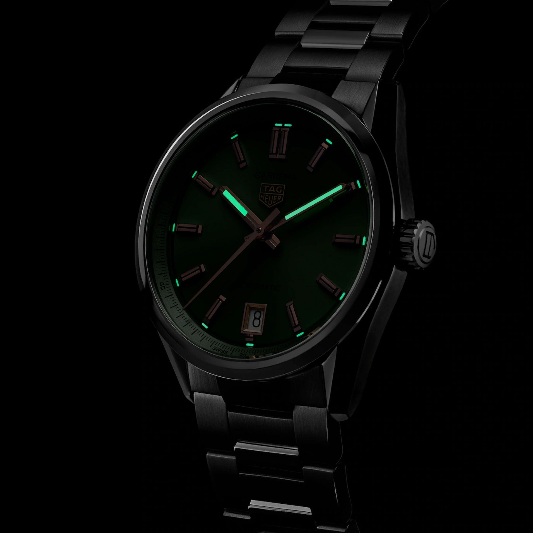 A TAG Heuer Carrera Date Automatic 36mm Watch in black, featuring luminous green hour markers and hands, stands out against a dark background. Crafted by TAG Heuer, this timepiece is powered by the precise Calibre 7 movement and displays the date at the 6 o’clock position.