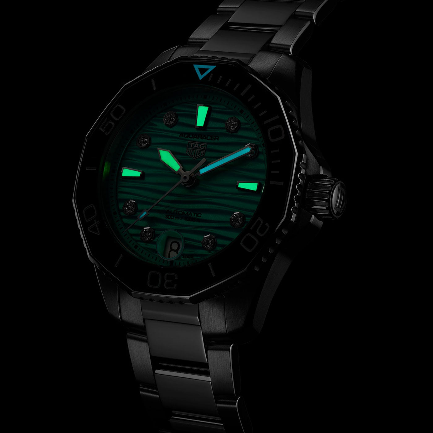 The TAG Heuer Aquaracer Professional 300 Date Automatic 36mm Watch features a green luminescent dial and hands that glow in the dark, illuminating the hour markers and indices. This automatic dive watch by TAG Heuer comes with a metal bracelet and bezel that maintain visibility even in low light conditions.