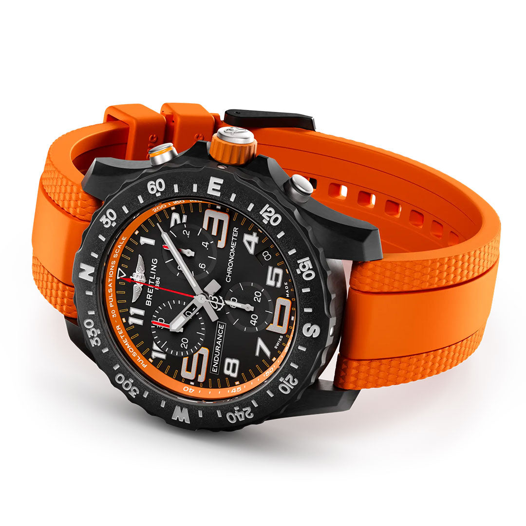 The BREITLING Professional Endurance Pro 44 is a sporty black watch with a textured bright orange rubber strap, white numerals, multiple subdials, date display, and a bold black bezel with white markings.