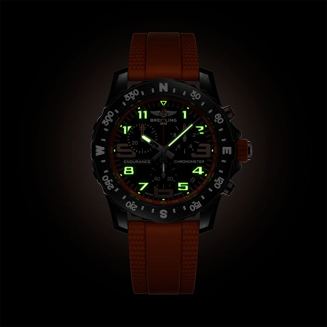 The BREITLING Professional Endurance Pro 44 is a black Breitling sports chronograph with a red textured strap, luminescent green and yellow numerals, compass bezel, and durable Breitlight—ideal as an athleisure watch against dark backdrops.