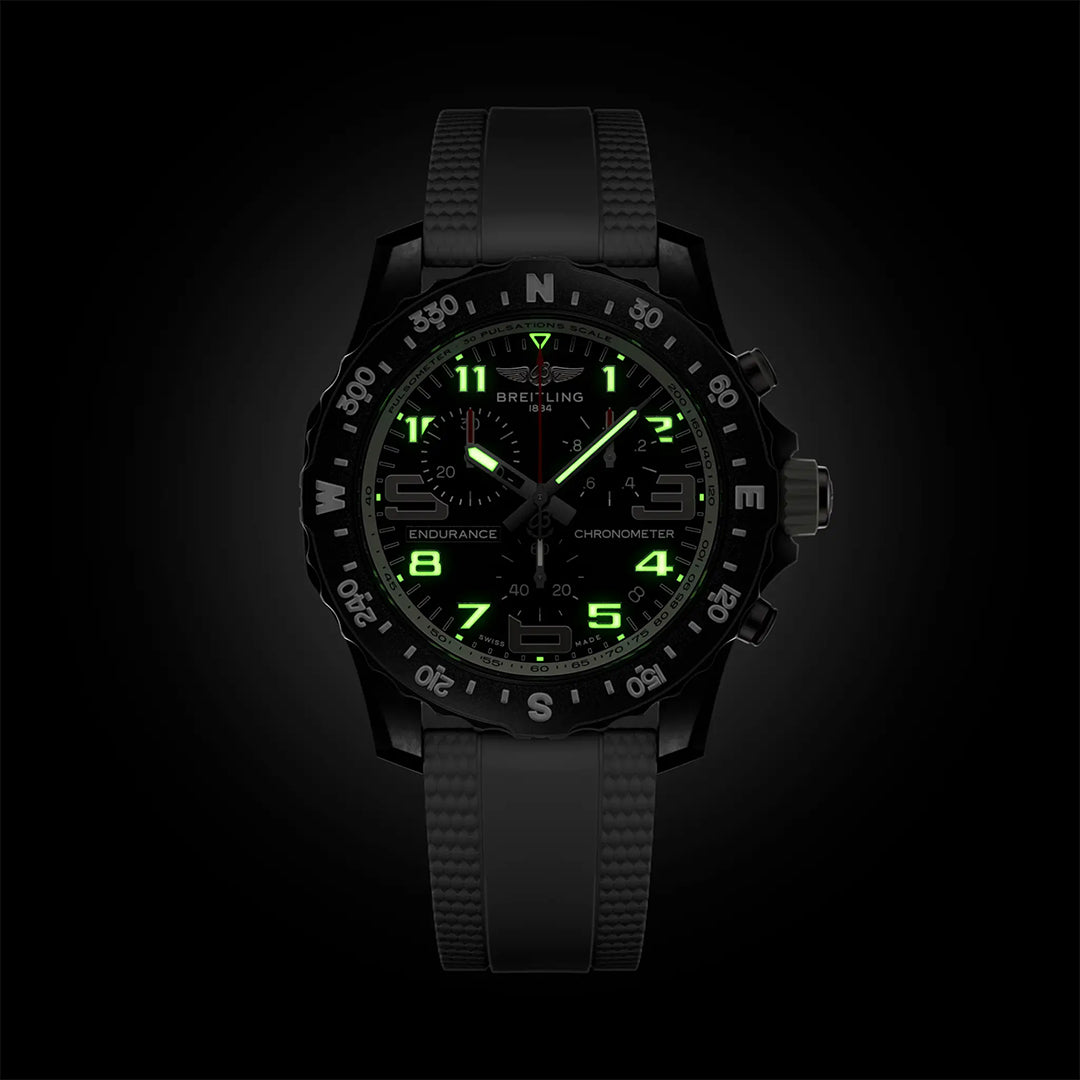 The Breitling Endurance Pro 44 is an athleisure watch in black, featuring a black strap, luminous green numerals, hands, and markers that glow in the dark. Its durable Breitlight® bezel shows white compass directions.