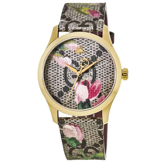 A Gucci G-Timeless Pink Blossom Quartz 38mm Watch featuring a gold case and a floral-patterned strap, complete with a matching dial. The design highlights pink and green flowers on a textured background, enhanced by minimalist hands that contribute to its elegant charm.