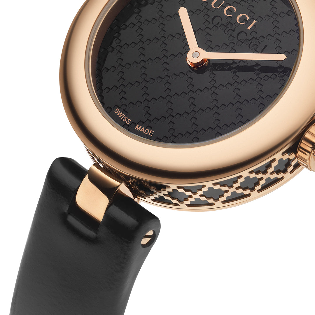 A detailed shot of a GUCCI Watch from the Diamantissima Quartz 27mm collection showcases its gold casing and black patterned face with gold hands. The case edge displays an intricate design similar to the iconic diamante pattern. Part of the black leather strap can be seen, and "Swiss Made" is inscribed on the watch face.