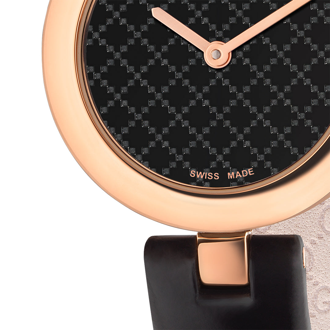 A close-up of the Gucci Diamantissima Quartz 27mm Watch showcases its exquisite rose gold case and black leather strap. The watch face displays a black, textured geometric pattern with "SWISS MADE" elegantly positioned at the bottom. Its minimalist hands embody the sophistication characteristic of GUCCI watches, making it a truly timeless accessory.