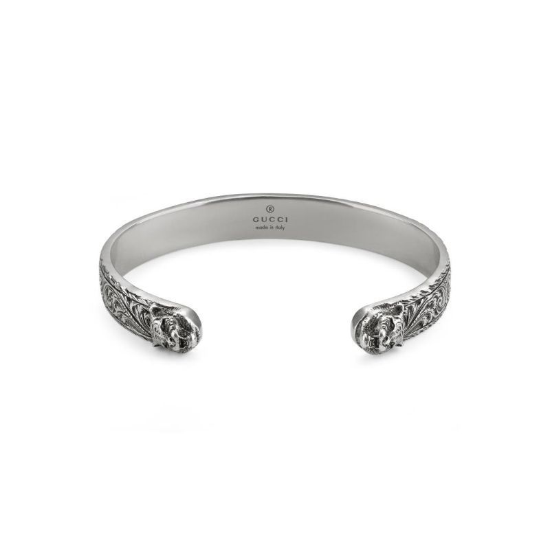 The Gucci Feline Head Sterling Silver Cuff Bracelet by GUCCI Fine Jewellery features detailed arabesque motifs along its band, with lion head designs at the open ends and an interior stamp reading "Gucci, made in Italy.