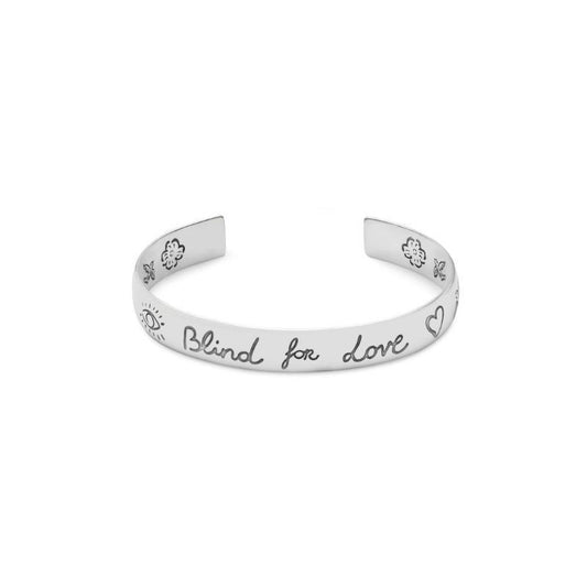 The Gucci Blind For Love Sterling Silver Cuff Bracelet from GUCCI Fine Jewellery highlights exquisite engraved designs of a sun, eye, and heart. The cuff is elegantly inscribed with "Blind for love" in black script across the front, making it a true masterpiece adorned with iconic Gucci motifs.