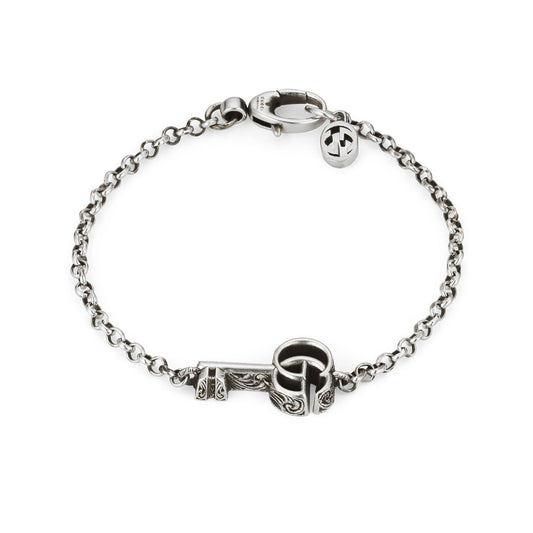 The Gucci Double G Key Sterling Silver Chain Bracelet by GUCCI Fine Jewellery showcases a delicate sterling silver chain with a central Double G key-shaped pendant. Featuring intricate ornamentation, the key exudes an elegant and vintage charm, while a small clasp completes this timeless piece.