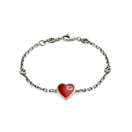 Introducing the Gucci Interlocking G Sterling Silver Station Bracelet from GUCCI Fine Jewellery, featuring a central red enamel heart pendant with a small circular logo. This elegant piece is completed with additional logo-embellished links and a lobster clasp closure.