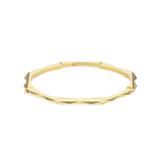 Introducing the Gucci Link to Love 18K Yellow Gold Studded Bangle from GUCCI Fine Jewellery, featuring a geometric design with angular facets for a modern and elegant aesthetic. This exquisite bracelet is presented on a simple white background.