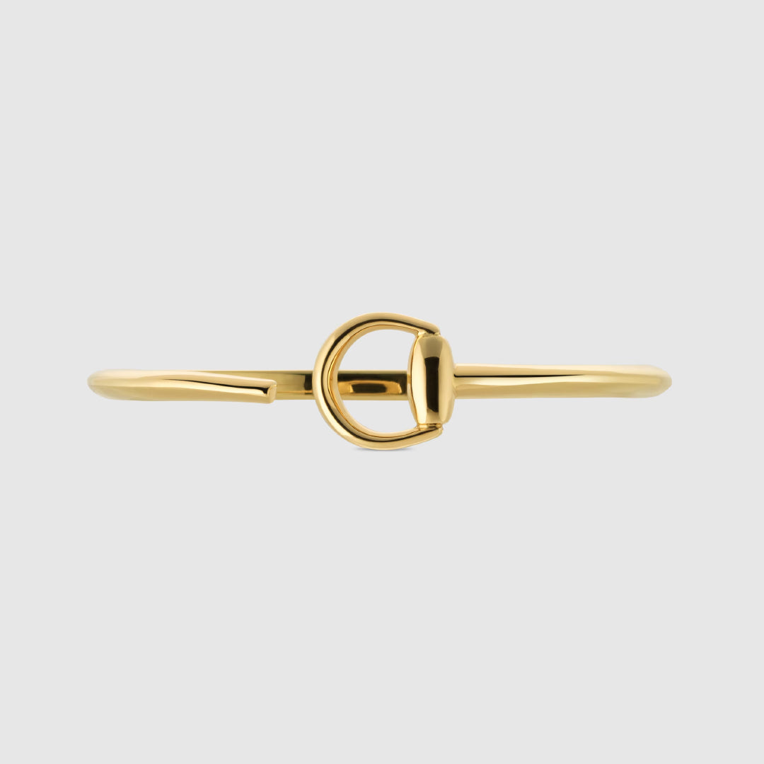 The Gucci Horsebit 18K Yellow Gold Cuff by GUCCI Fine Jewellery, featuring a polished finish and signature D-shaped clasp, is shown against a plain light gray background.