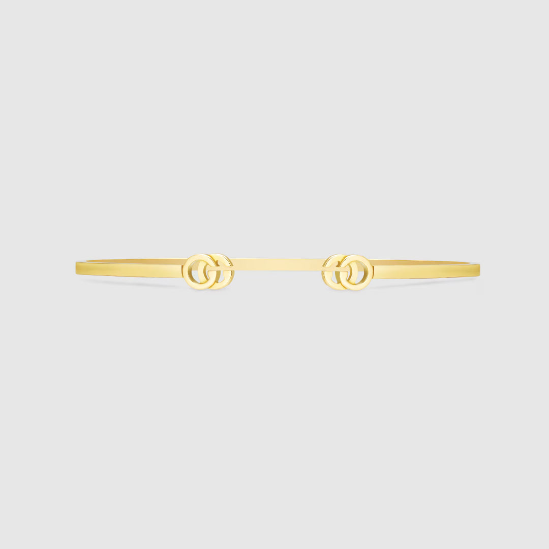 A sleek Gucci GG Running 18K Yellow Gold Cuff from GUCCI Fine Jewellery, featuring interlocking Double G logos, showcased on a plain light gray background.