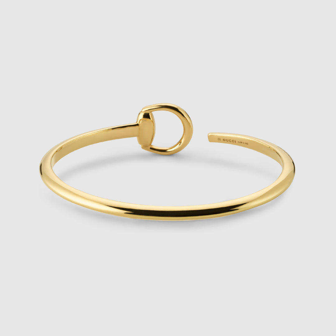 The Gucci GG Running 18K Yellow Gold Cuff by GUCCI Fine Jewellery showcases a sleek, circular minimalist design with a small ring detail, displayed on a light gray background—an elegant choice for responsible jewelry lovers.