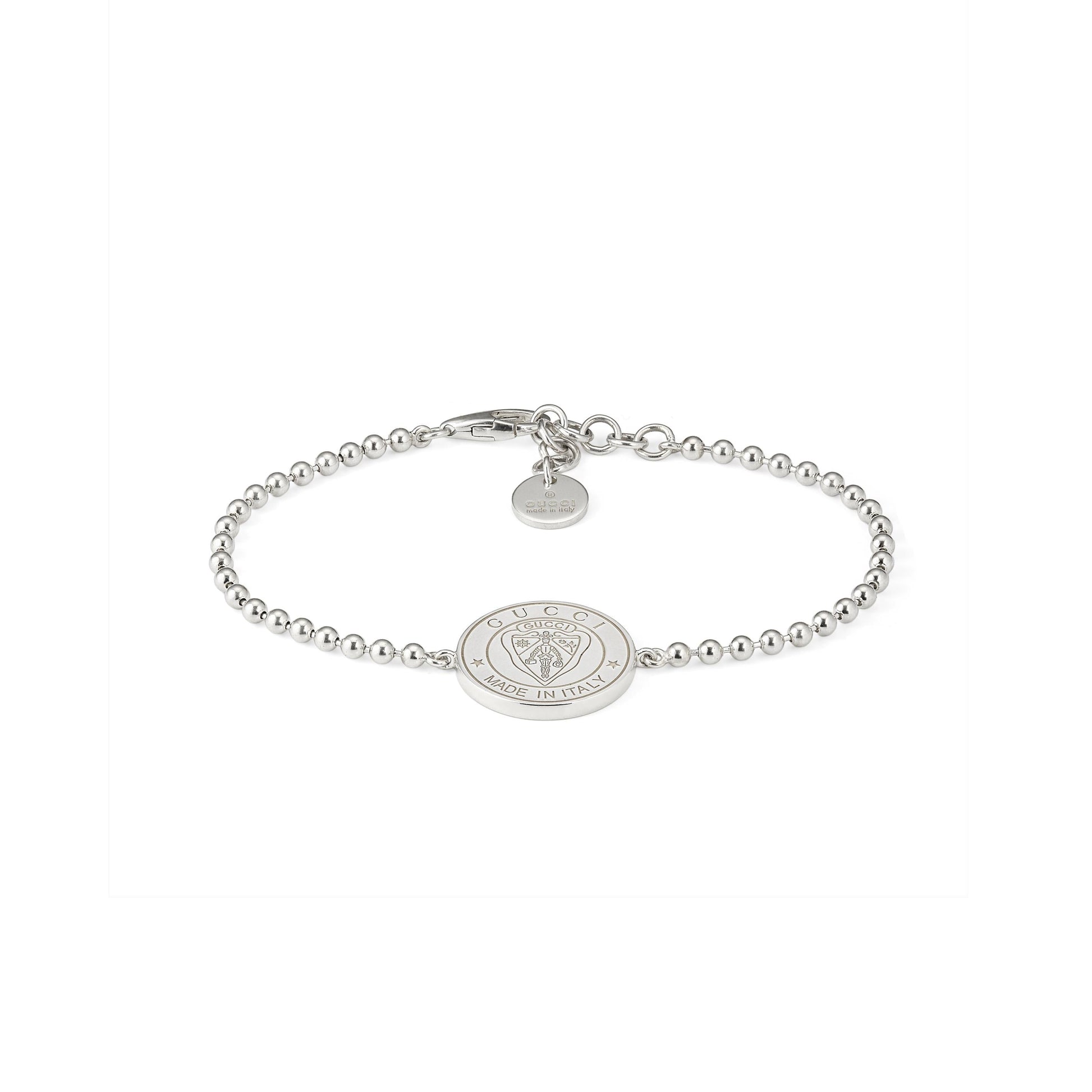 The Gucci Crest Sterling Silver Boule Bracelet by GUCCI Fine Jewellery features 925 sterling silver beads, a central engraved crest charm, and a small round tag near the clasp, all in a minimalist design. Displayed on a white background.