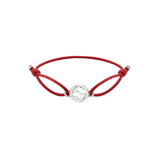 The Gucci Interlocking Cotton Cord with Sterling Silver Bracelet by GUCCI Fine Jewellery features a red cord and a silver-toned circular charm with the iconic Interlocking G logo, plus adjustable side knots for a perfect fit.