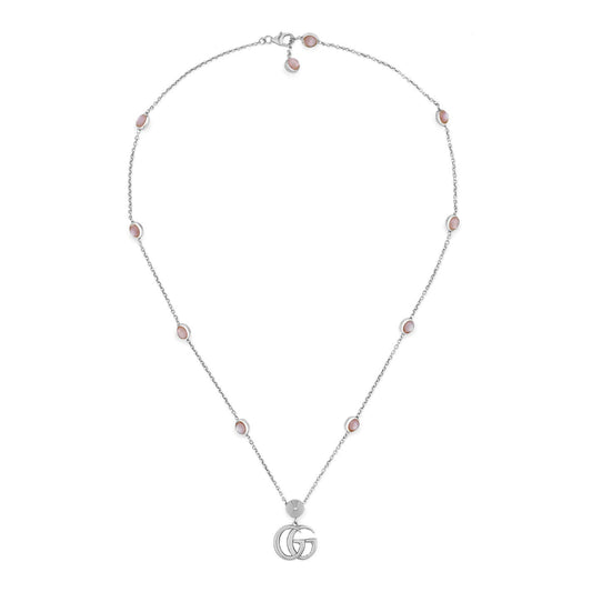 The GUCCI Fine Jewellery piece, the Gucci Double G Pink Mother of Pearl Sterling Silver Station Necklace Pendant, showcases a sterling silver chain embellished with small, round pink mother of pearl stones evenly arranged along its length. Centrally placed is an iconic Double G pendant. The necklace is gracefully presented in an open loop against a white background.