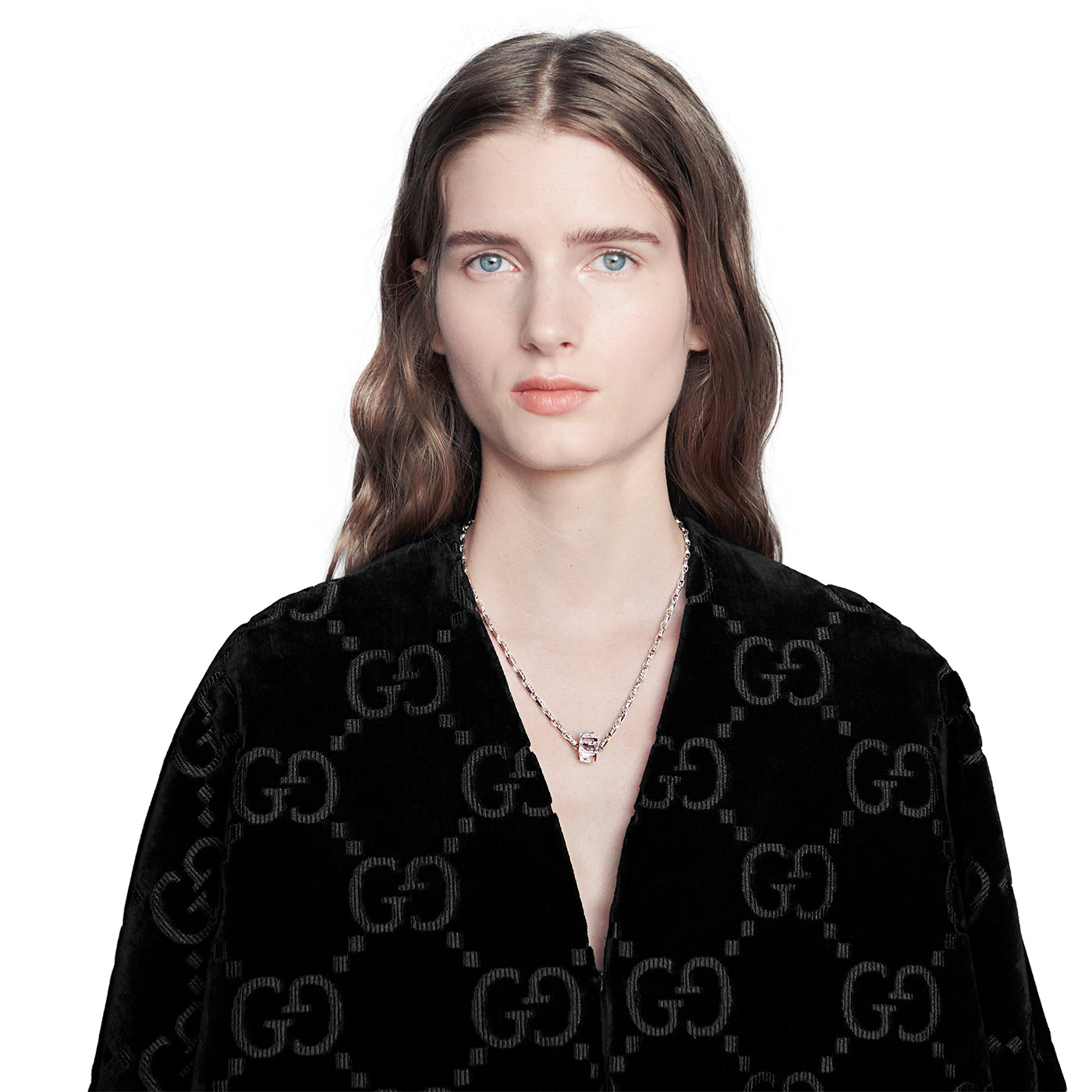 A person with long hair wearing a black patterned jacket stands against a plain background, showcasing their Gucci G Cube Sterling Silver Necklace from GUCCI Fine Jewellery.