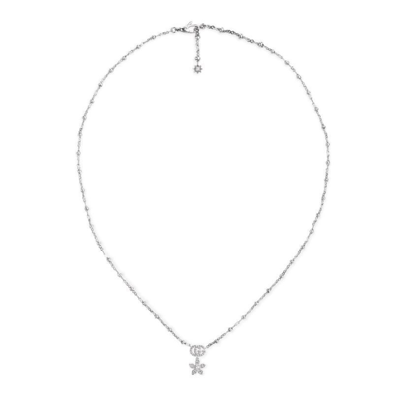The Gucci Flora 18K White Gold Diamond Necklace Pendant by GUCCI Fine Jewellery shines brilliantly against a plain white background, featuring a delicately diamond-encrusted cross pendant. A small decorative element elegantly dangles from the clasp on the chain, enhancing its charm.