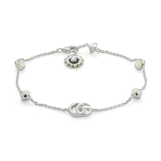 The Gucci GG Marmont Mother of Pearl Sterling Silver Bracelet by GUCCI Fine Jewellery is a delicate sterling silver chain bracelet featuring a central Double G emblem. It includes small round charms and a daisy charm with a lustrous mother-of-pearl center, and is secured with a lobster clasp.