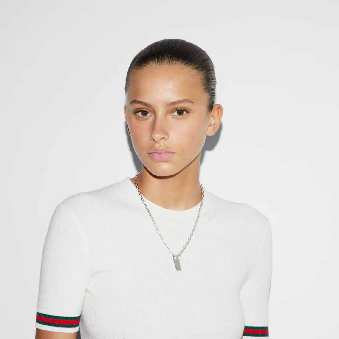 A person with their hair pulled back wears a white shirt and the Gucci Trademark Sterling Silver Chain Necklace Pendant with Padlock from GUCCI Fine Jewellery, posing against a plain white background. Their expression is neutral, and they are looking directly at the camera, embodying the sleek elegance of Pre-Fall 2024.