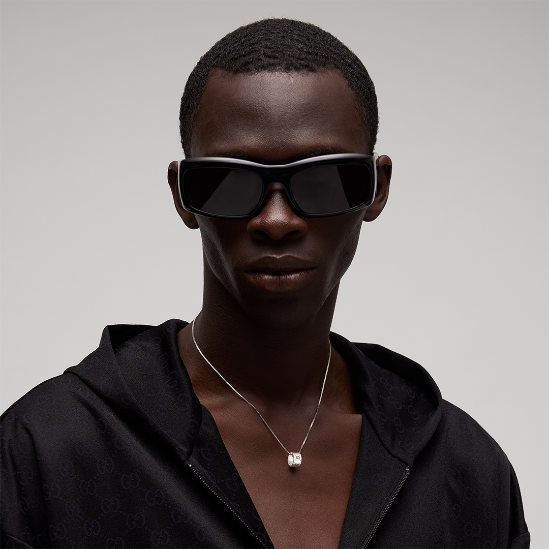 A person wearing black sunglasses and a Gucci Signature Sterling Silver Necklace Pendant.