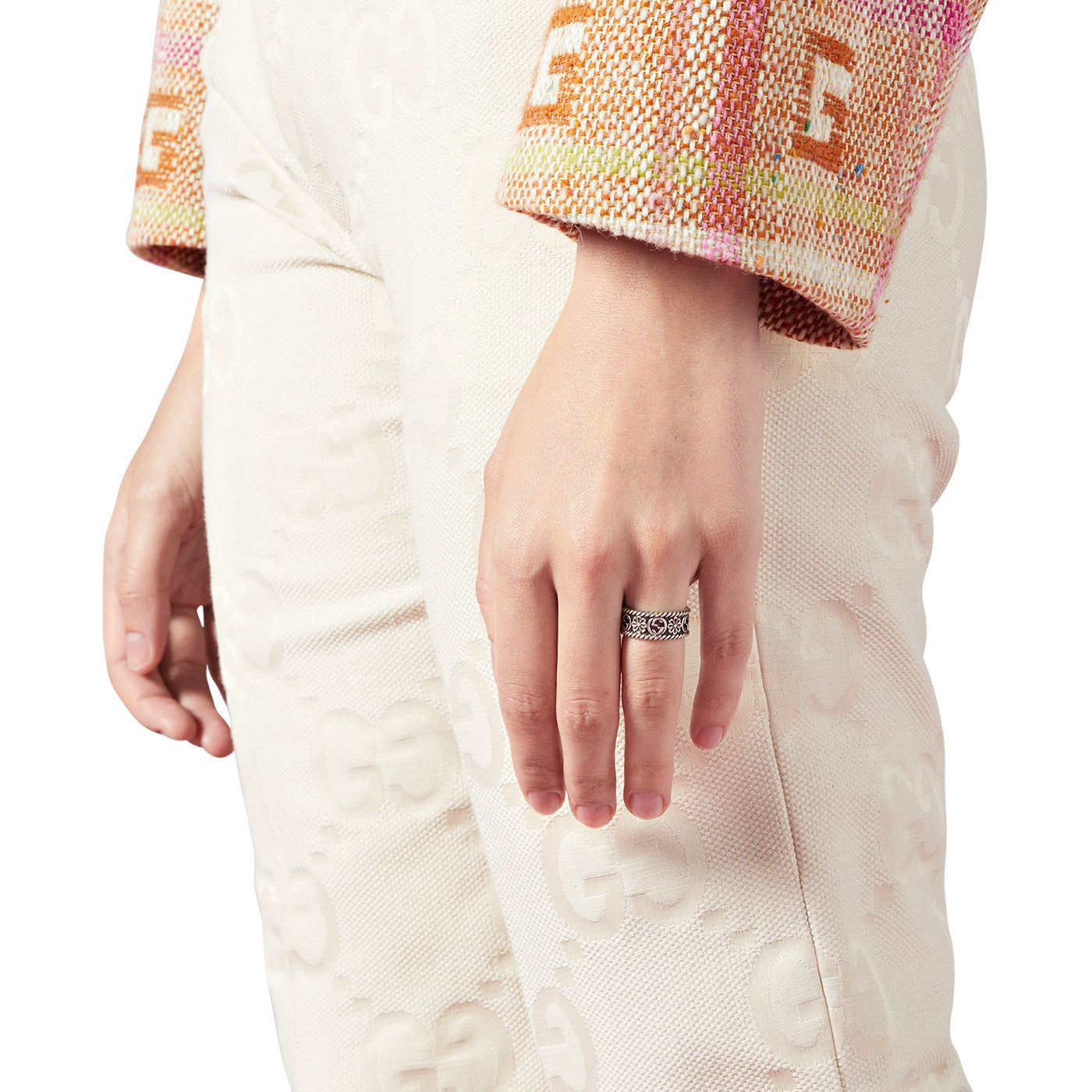 A person is wearing a textured multicolored jacket and patterned white pants, highlighting their left hand adorned with the Gucci Interlocking G Sterling Silver Ring from GUCCI Fine Jewellery, emphasizing the elegant Interlocking G design.