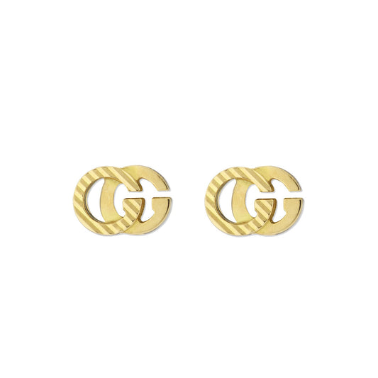 The Gucci Running G 18K Yellow Gold Stud Earrings by GUCCI Fine Jewellery exemplify elegance with their interlocking double G design, featuring one earring for each ear. They boast a striped pattern on overlapping sections, creating a minimalist and symmetrical look that stands out beautifully against a plain white background.