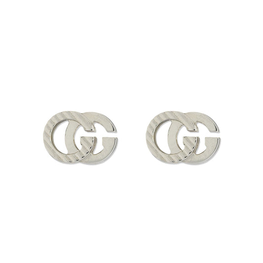 The Gucci Running G 18K White Gold Stud Earrings from GUCCI Fine Jewellery showcase interlocking "G" letters in a shiny, textured finish. Crafted from white gold, these stud earrings stand out against a plain white background.