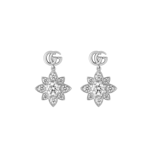These Gucci Flora Double G 18K White Gold Diamond Stud Earrings from GUCCI Fine Jewellery feature an elegant floral design. Each earring showcases a central sparkling gem encircled by small diamond-like stones, with two interlocking "G" symbols above the intricate diamond flowers, capturing the signature Gucci Flora elegance.