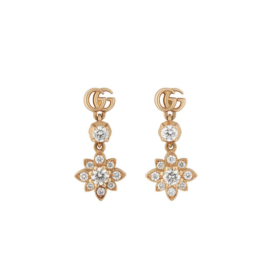 The Gucci Flora Double G 18K Rose Gold Diamond Stud Earrings by GUCCI Fine Jewellery are expertly crafted in 18K rose gold and prominently display a logo at the top. They highlight a small round gem and an elegant flower-shaped design embellished with multiple sparkling gemstones dangling below.
