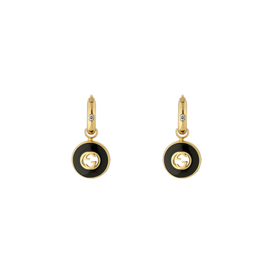 Featuring the Gucci Interlocking G 18K Yellow Gold and Black Onyx Hoop Earrings by GUCCI Fine Jewellery, these gold hoops showcase black onyx circular pendants with a cut-out Interlocking G design. Each hoop is adorned with a small clear gemstone at the top, beautifully displayed against a plain white background.