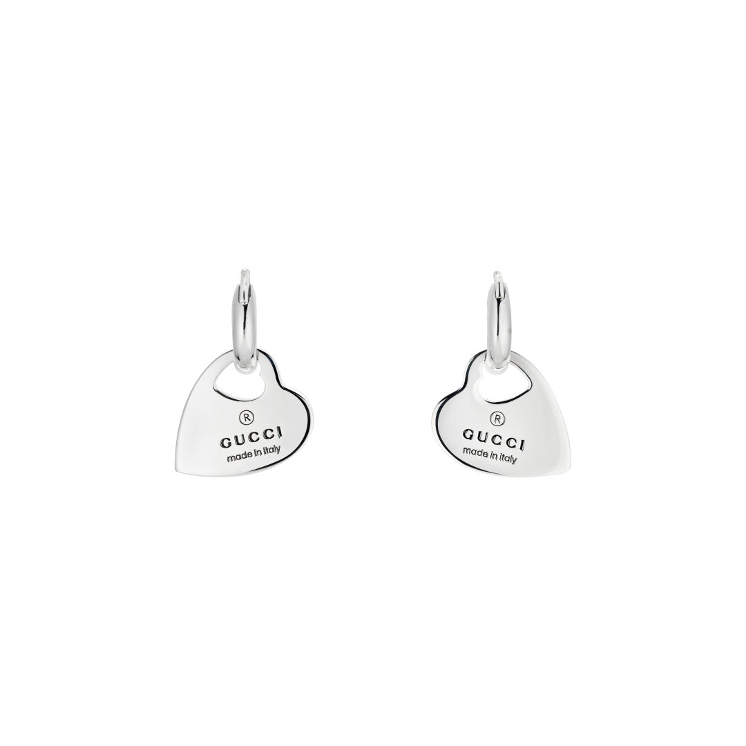 The Gucci Trademark Sterling Silver Hoop Earrings from GUCCI Fine Jewellery showcase heart-shaped pendants inscribed with the Gucci logo and "made in Italy." These earrings exhibit a sleek, polished design against a plain white background.