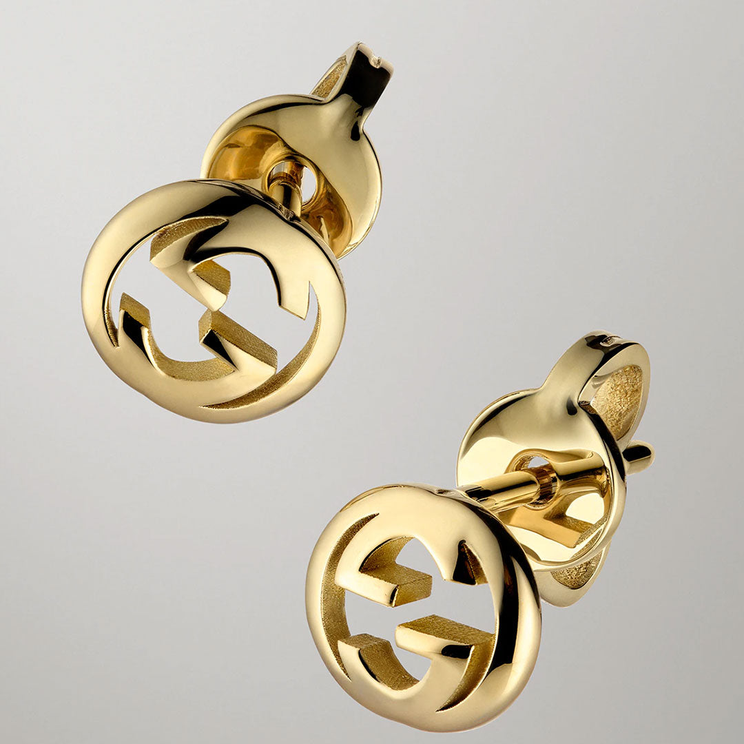 GUCCI Fine Jewellery Interlocking G 18K yellow gold stud earrings feature a polished, shiny finish and a round, open-cut design with the iconic interlocking “G” logos, displayed against a plain light gray background.